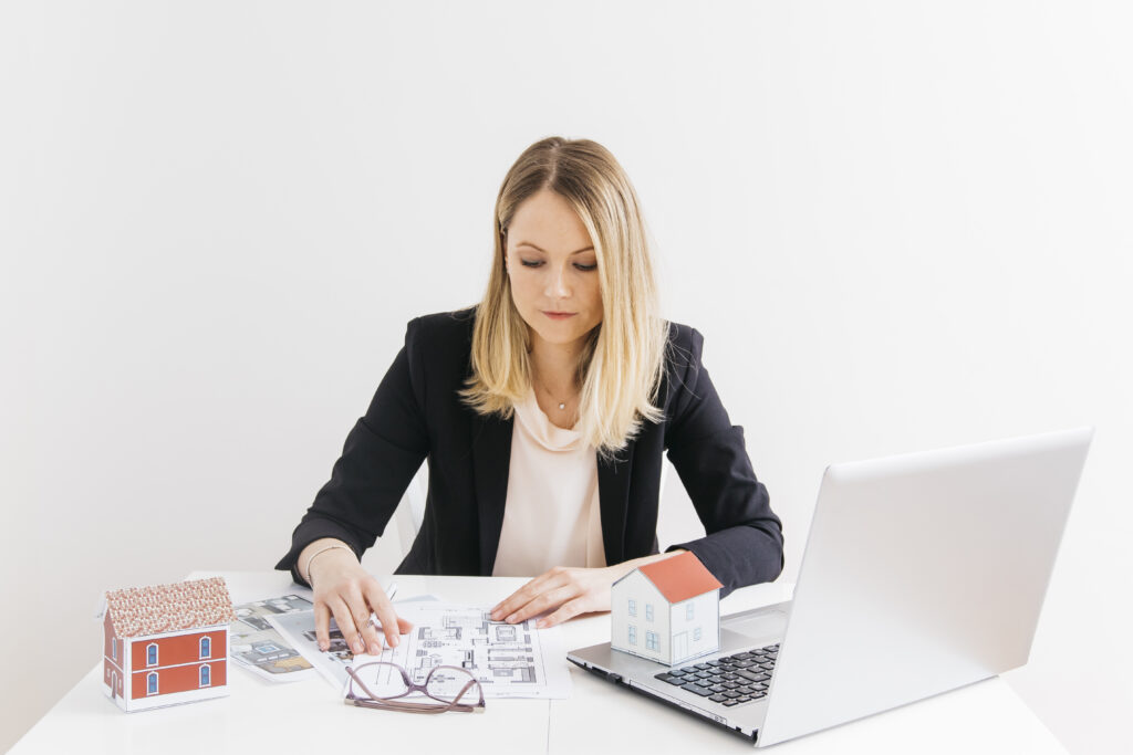 businesswoman-siting-front-laptop-looking-blueprint-office